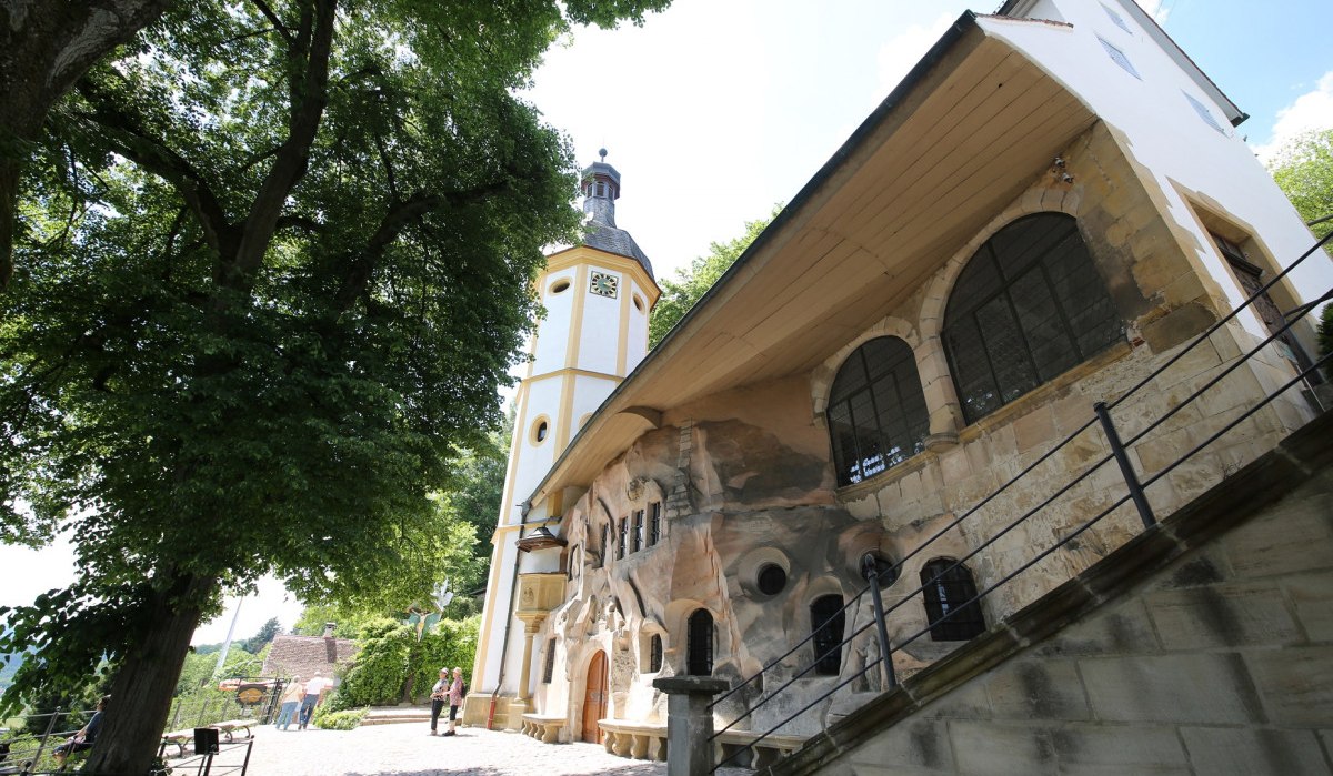 Felsenkapelle St. Salvator. Im Hintergrund stehen zwei Wanderer. Zwei Personen laufen aus dem Bild. Vor der Kapelle steht ein großer grüner Baum., © Foto: Walter Laible