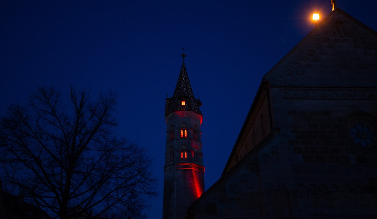 Es ist Nacht, der Himmel ist dunkelblau, der Johannisturm wird mit rotem Licht beleuchtet.  Neben dem Turm steht ein Baum., © Foto: Mario Klaiber