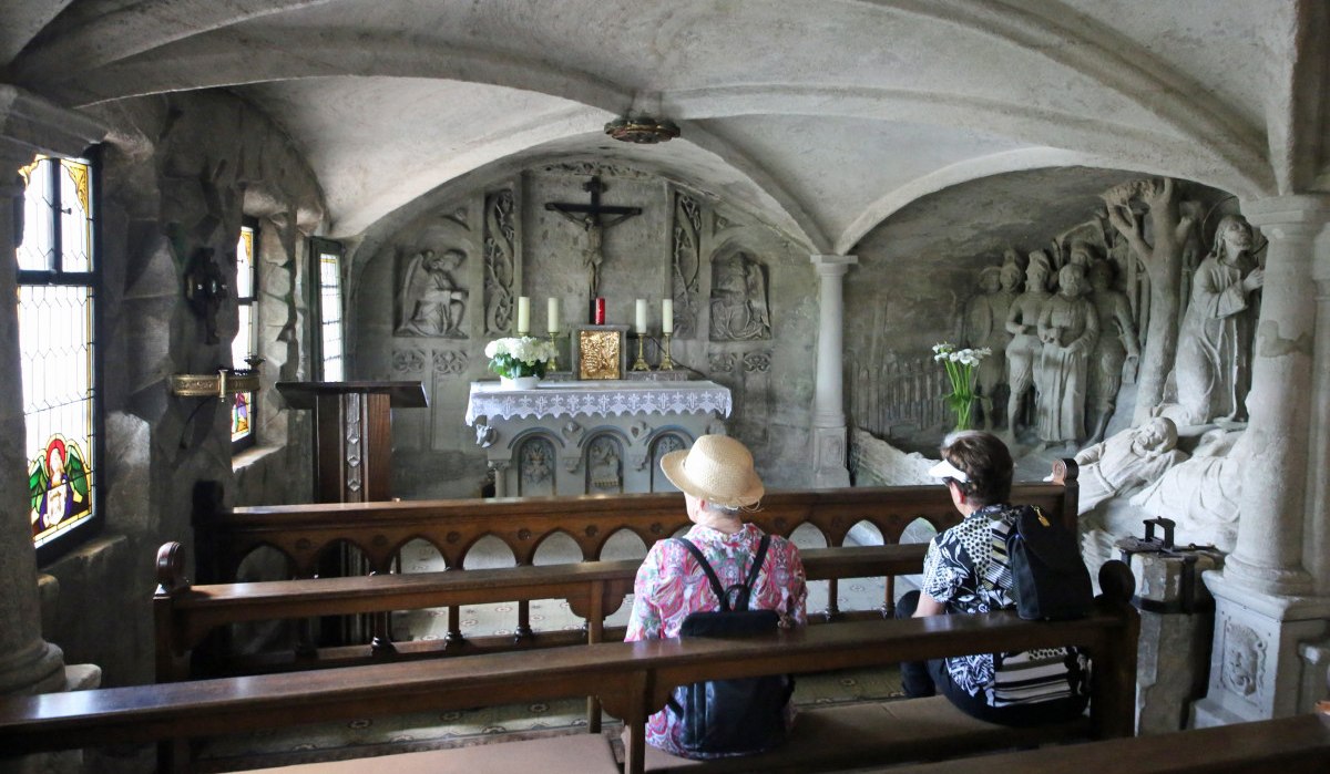 Zwei Personen sitzen auf Kirchenbänken in der Felsenkapelle und schauen auf den Altar., © Touristik- und Marketing GmbH